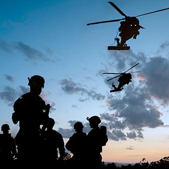 黄昏时战场上五名士兵的剪影，两架直升机在上空盘旋